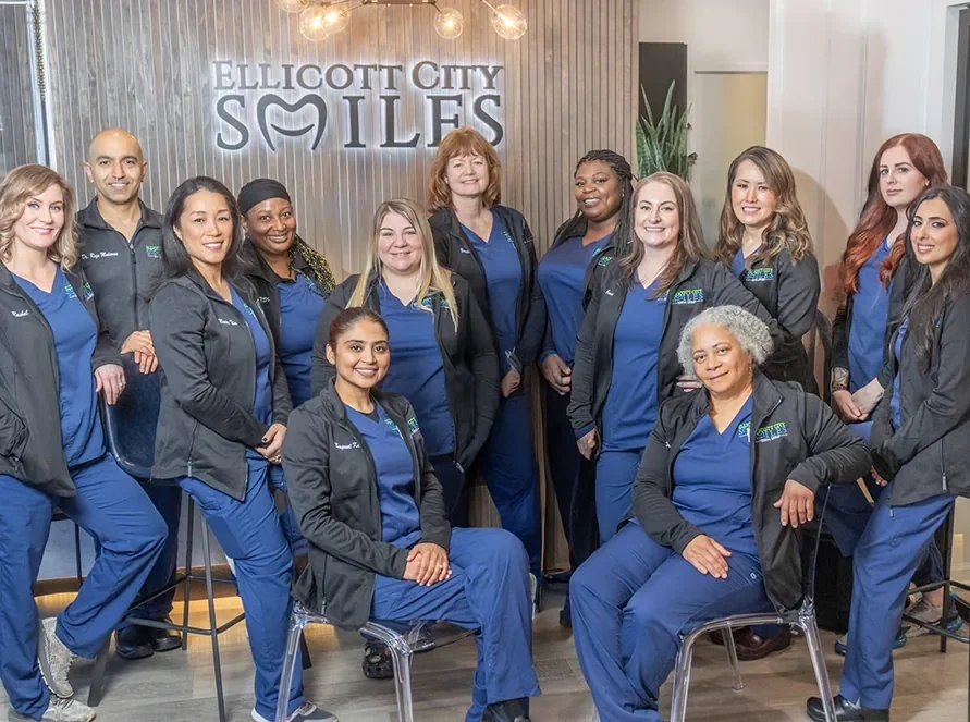 The Ellicott City Smiles dentists and team together in front of the sign wall inside the office.